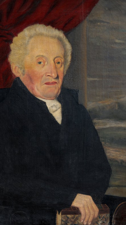 Portrait of Samuel Reichel. A man, seated, in a dark jacket, with a red curtain in the background.